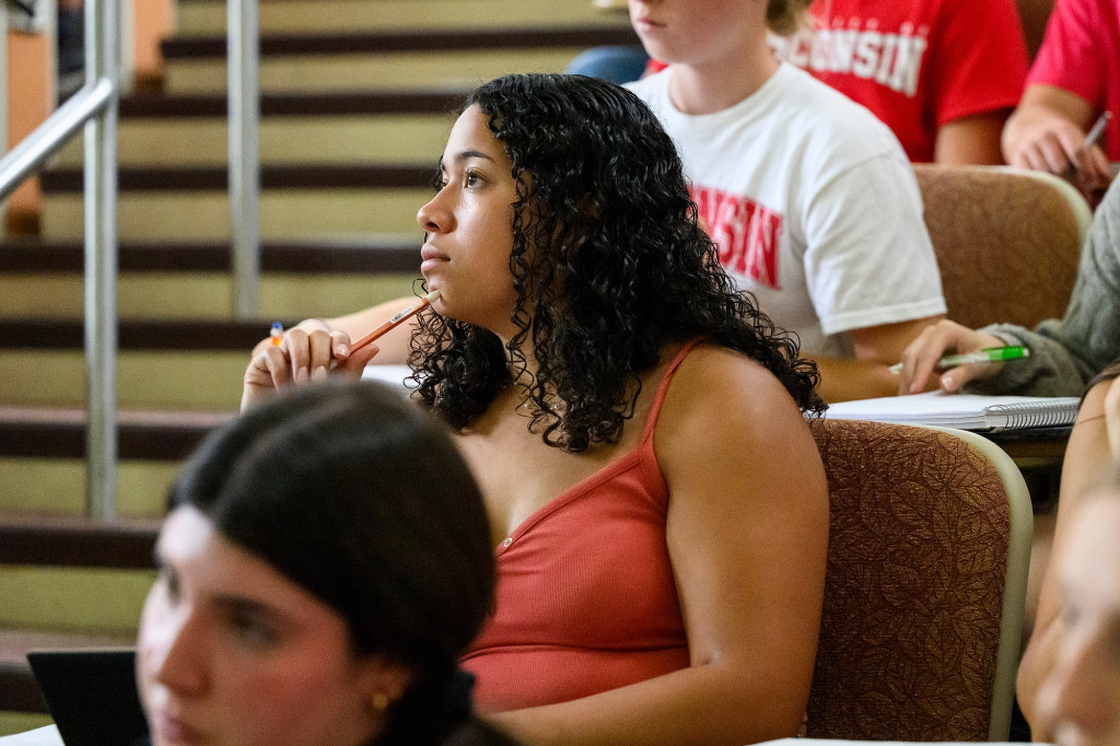 A close shot of a woman holding a pencil to her chin as she looks thoughtfully off camera.