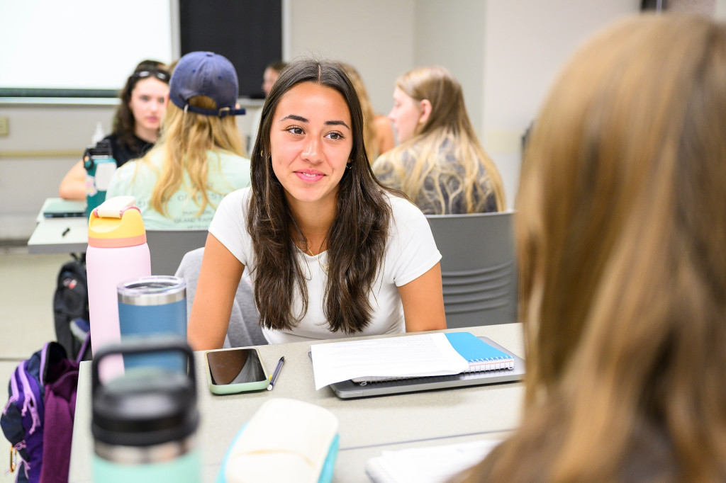 A woman talks to a classmate across a table.