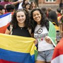 Two people are arm in arm, while holding up flags.