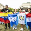 Four people stand in a row holding up flags.