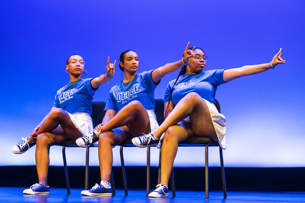 Several women sitting in chairs cross their legs and gesture with their hands.