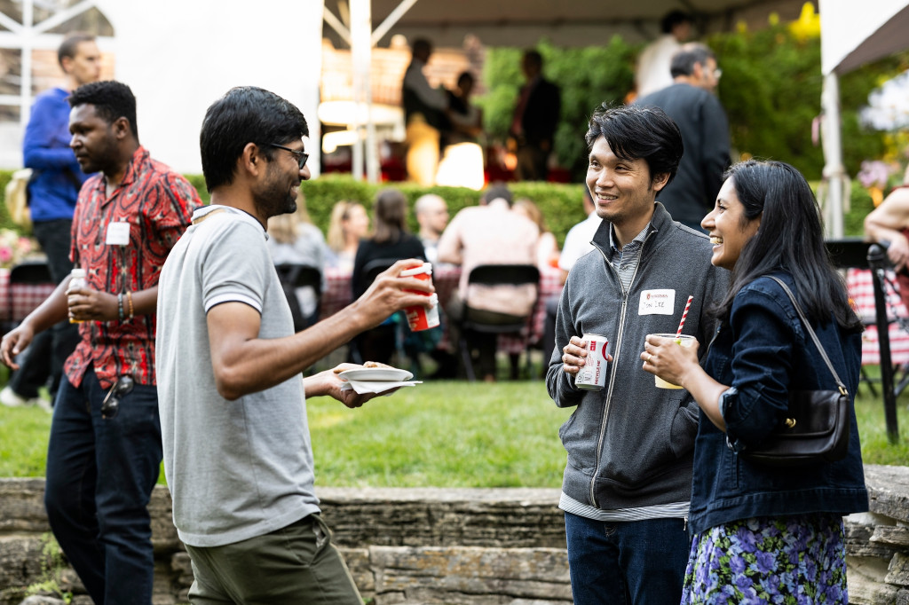 Several people holding drinks and standing talk at a party.