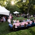 A wide view of people sitting and eating at picnic tables on the lawn at Olin House.