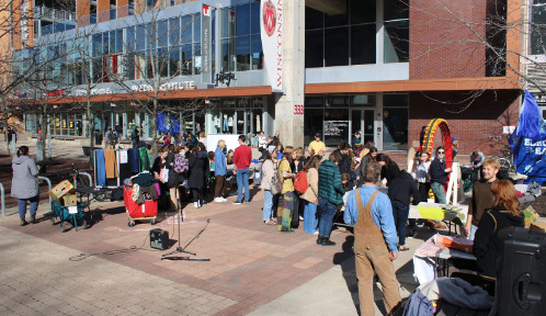 People gather in a plaza outside a building, where there's a microphone stand for those who want to speak.