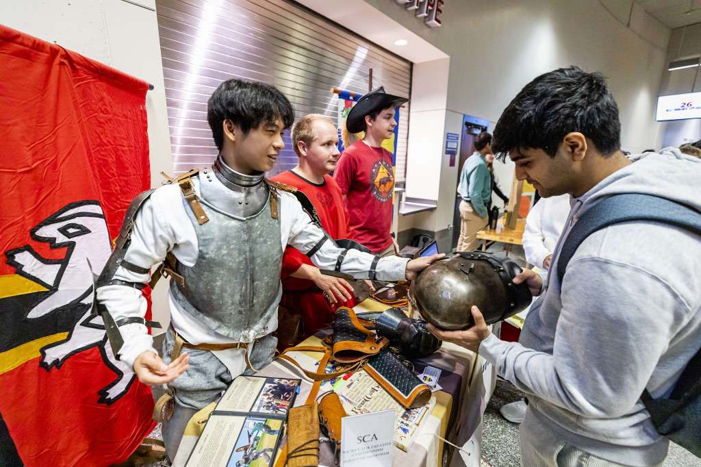 A person wearing old-fashioned knight's armor talks to another.