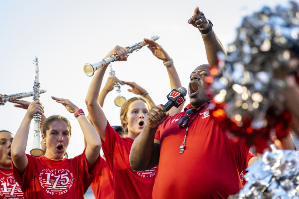 Corey Pompey makes an O sign above his head with his arms, and several clarinet players from the marching band join him.