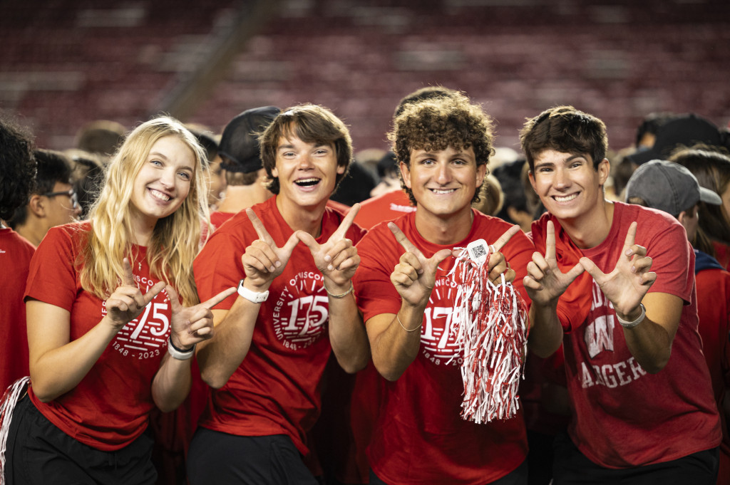 In the crowd, four students smile and make W signs toward the camera.