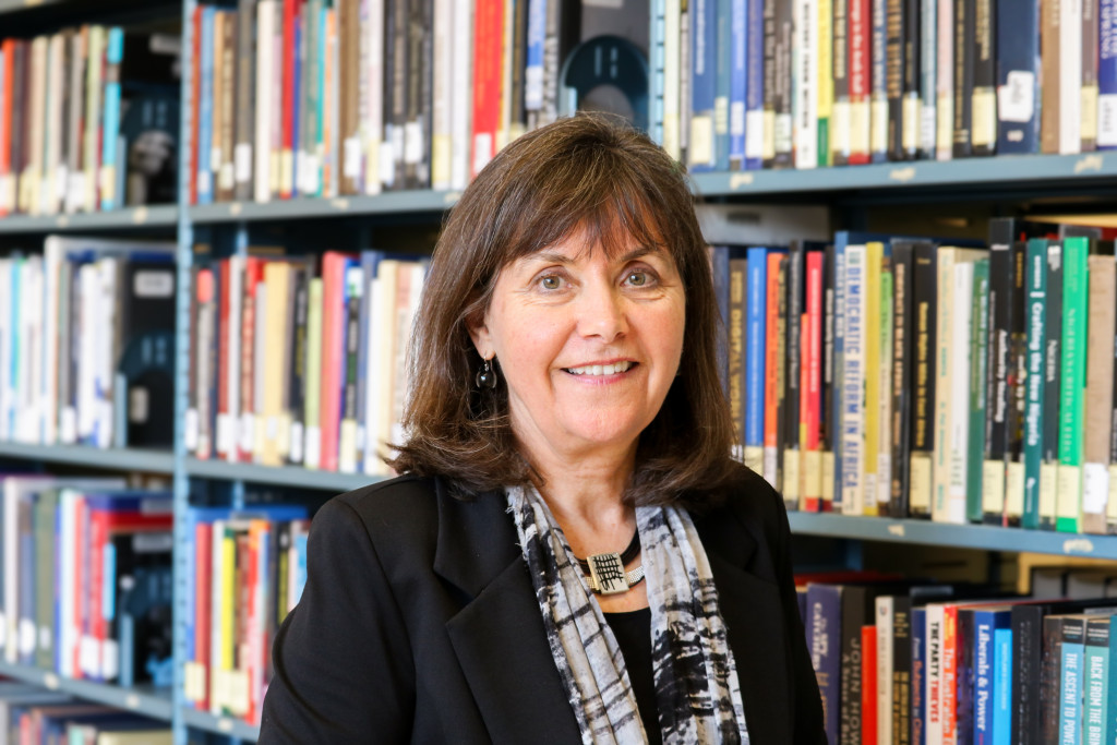 A photo portrait of Erla P. Heyns standing in front of library shelves filled with books.