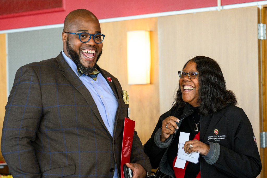 A man and a woman stand side by side with beaming smiles on their faces.