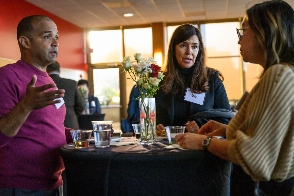 Three people in a crowded reception room stand in conversation at a cocktail table.