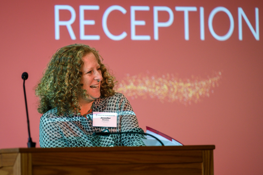 Jennifer Mnookin speaks with a smile on her face as she addresses the room from a podium. Behind her, a screen reads Faculty of Color Reception.