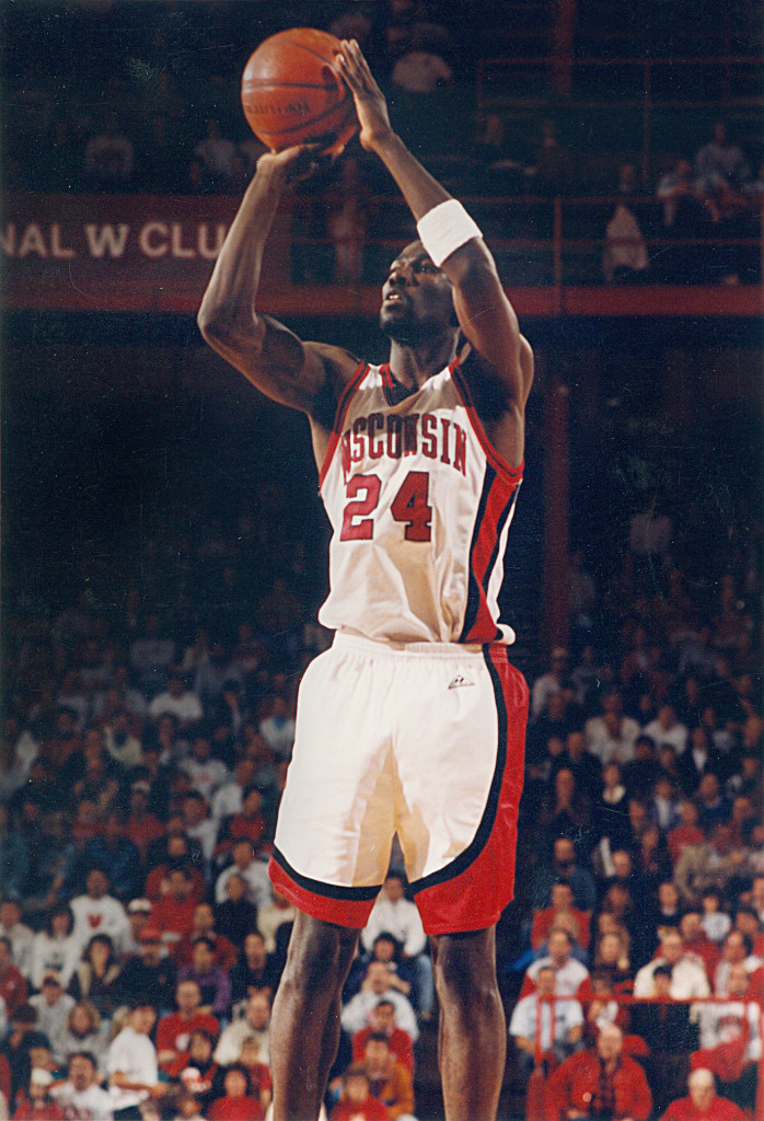 A man in a Wisconsin uniform stands and takes a free throw.