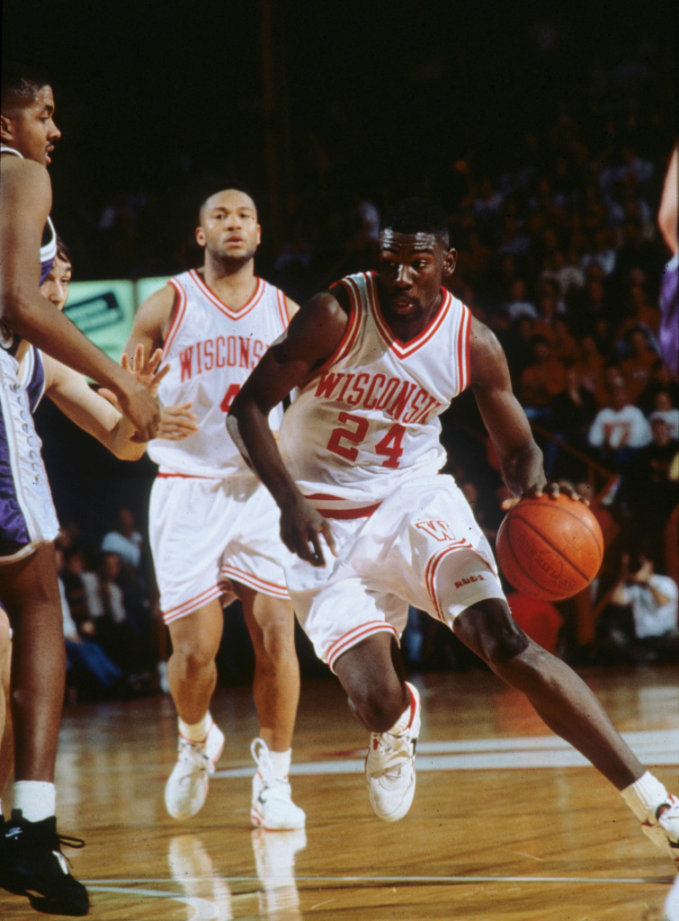 A man in a Wisconsin jersey dribbles past opposing players.