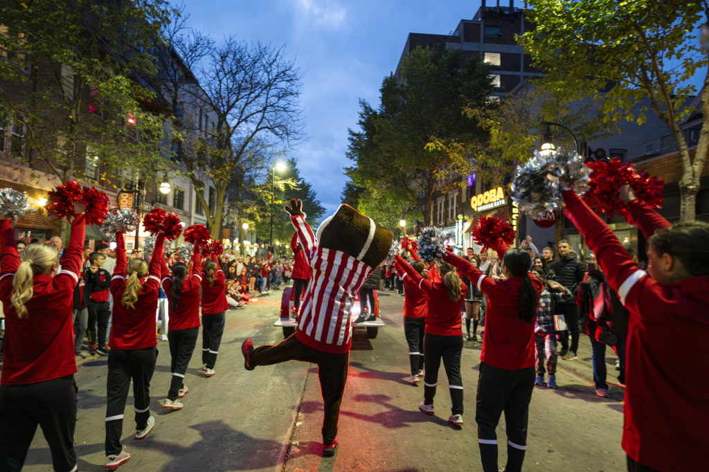 Facing away from the camera, Bucky Badger and the UW Spirit Squad parade down State Street in twilight to celebrate Homecoming.