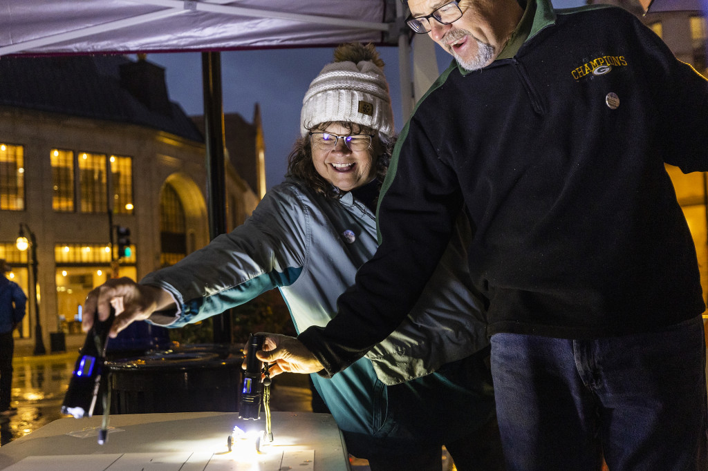 Two people smile as they show off a solar car.