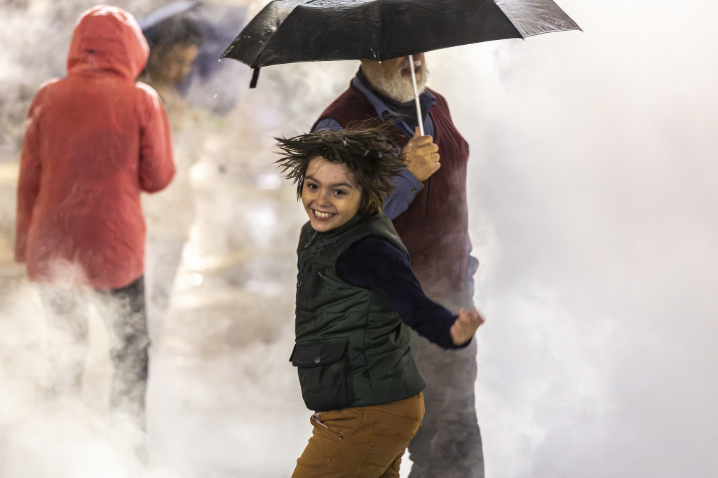 A child dances in some steam as others stand by.