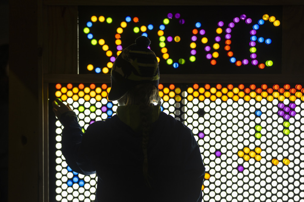 A silhouetted person puts up lights on a board.