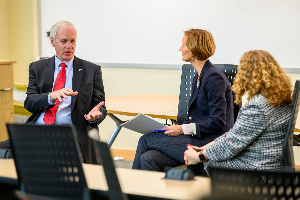 Three people talk in front of a classroom.