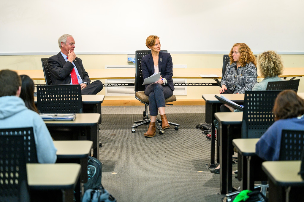 Three people sit at a table in front of a classroom.