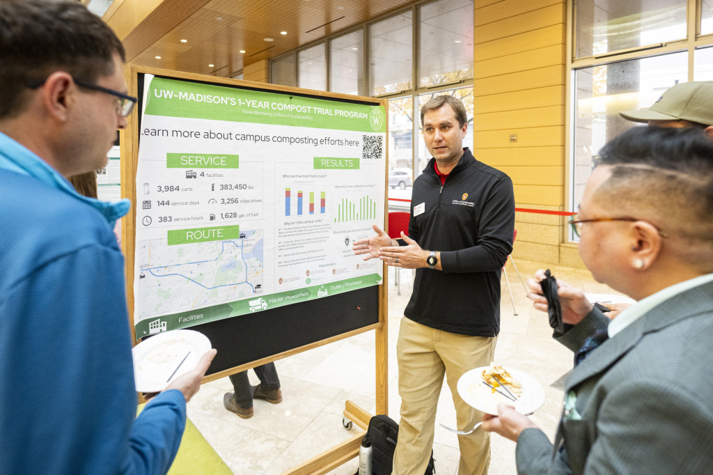 A man stands in front of a poster and talks to others.