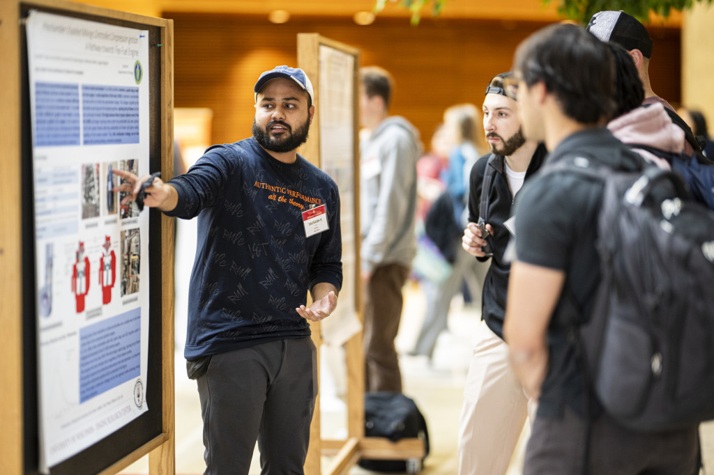 A man stands in front of a poster and talks to others.