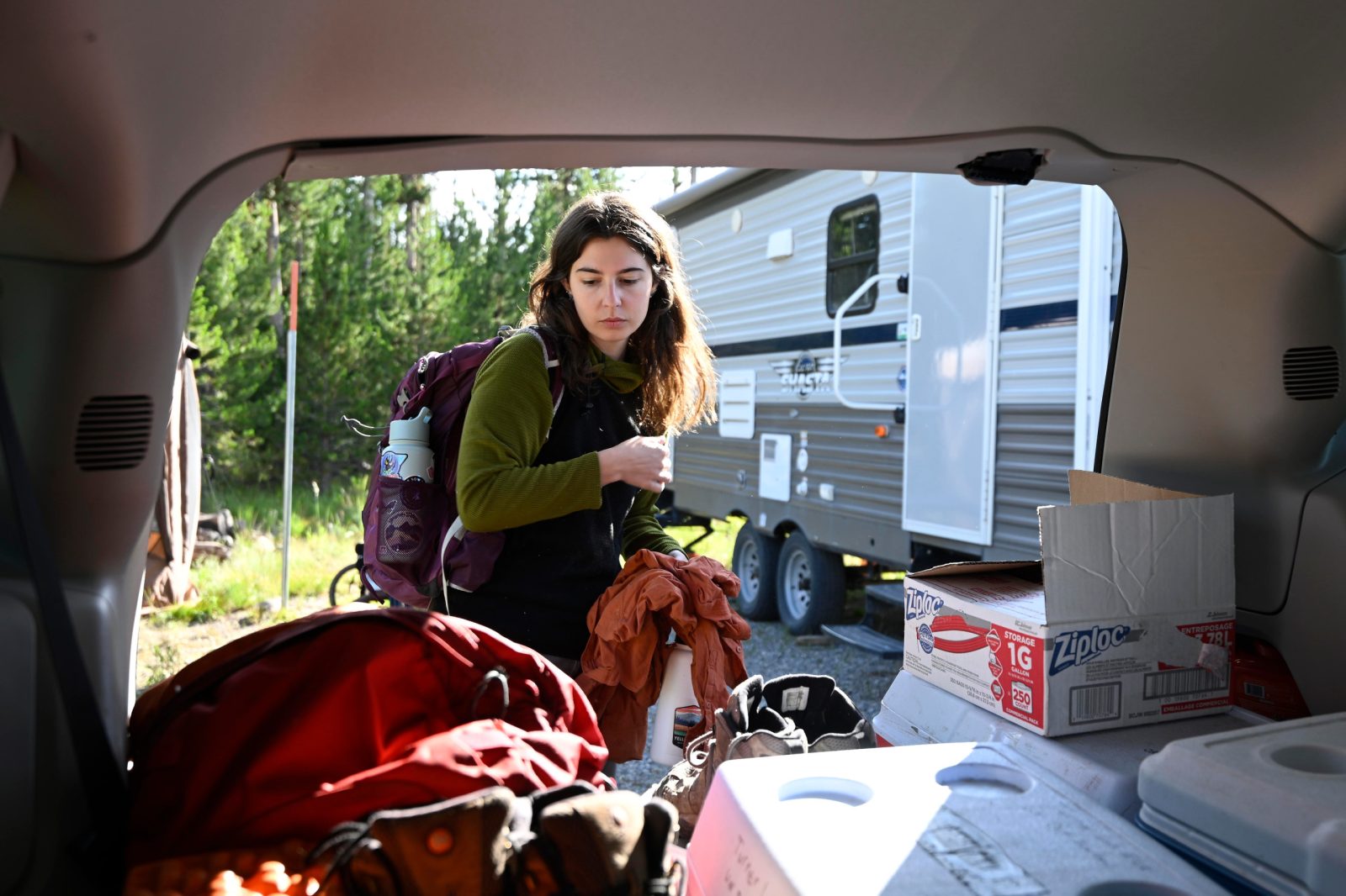 A woman wearing a backpack looks at field gear in the back of a minivan