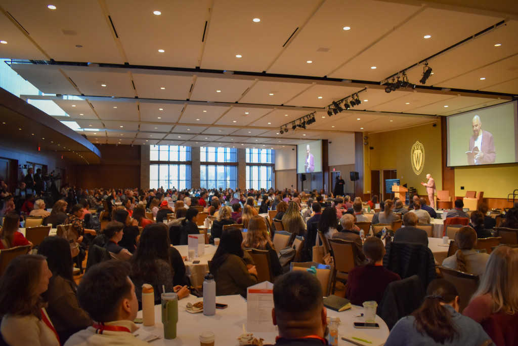 A hall filled with people listening to a speaker.