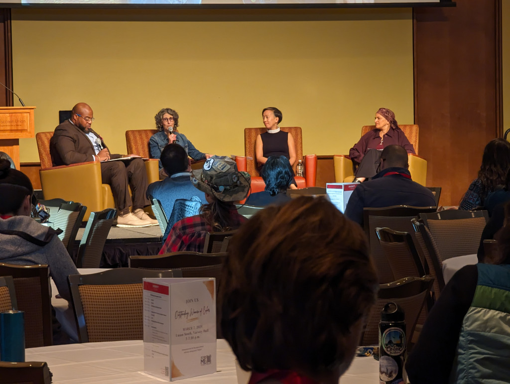 Four people sit in chairs on a stage, and one talks.