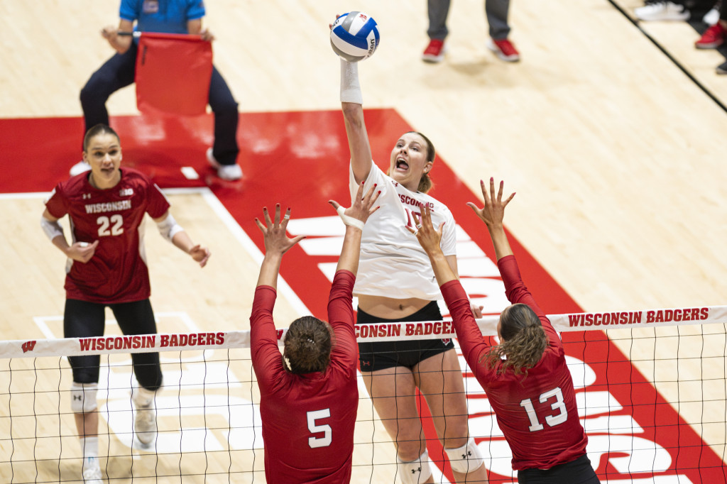 A volleyball player in a Wisconsin uniform tips the ball over the net.