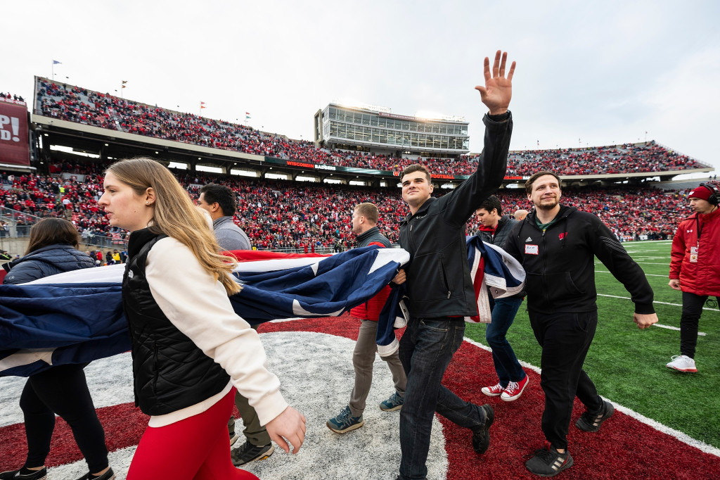 A group of people smile and wave as they come onto the football field.