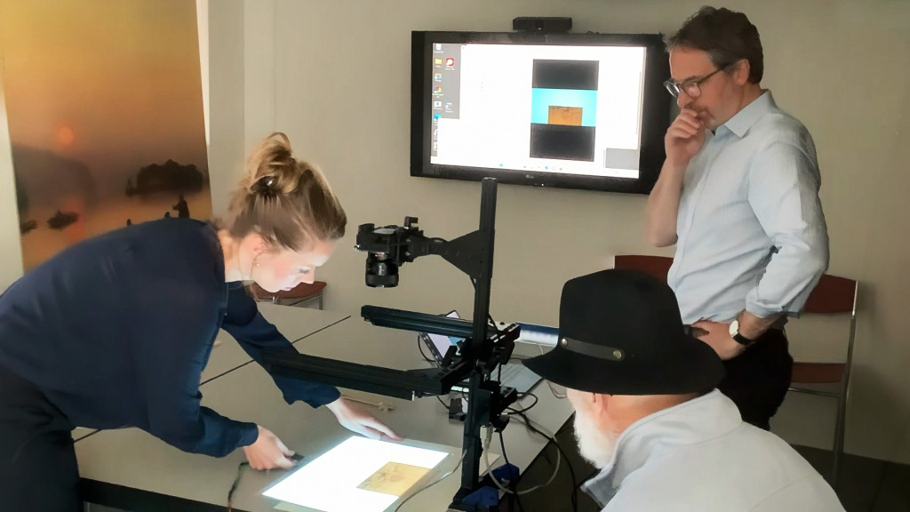 Several people place old documents on a scanning device.