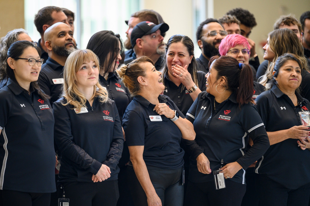 A group of about 20 UW Recreation & Wellbeing staff stand together in a tight group. They're laughing and talking as they look around at the newly-opened Bakke Recreation and Wellbeing Center.