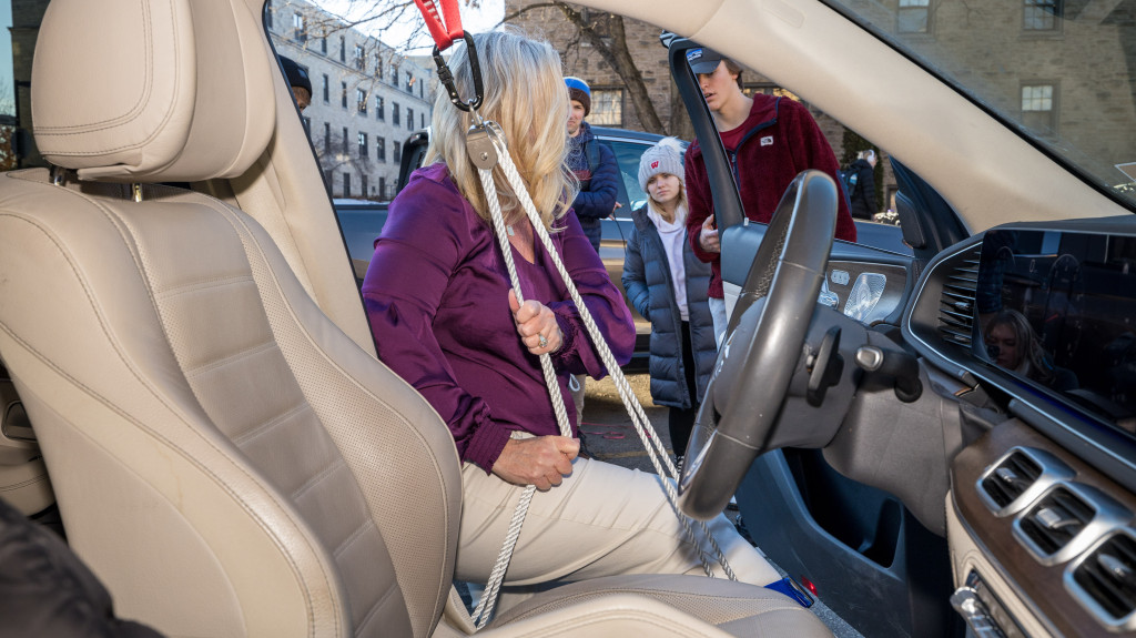 A woman uses a pulley system to enter a car.