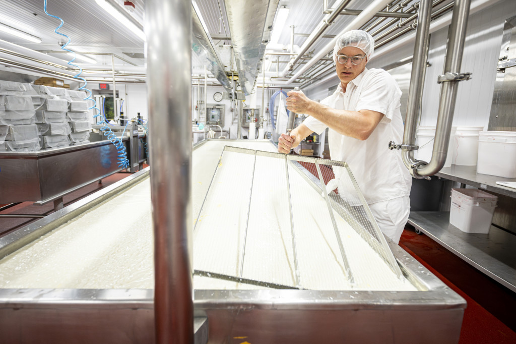 A person passes a big metal instrument through goopy milk mixture.