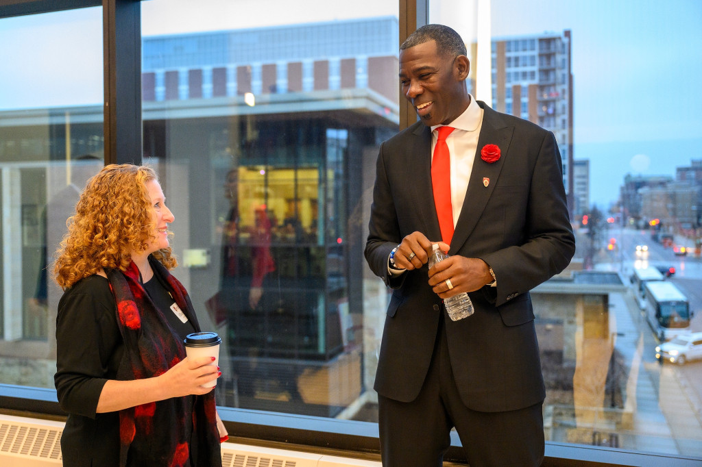 Two people talk in front of a window.