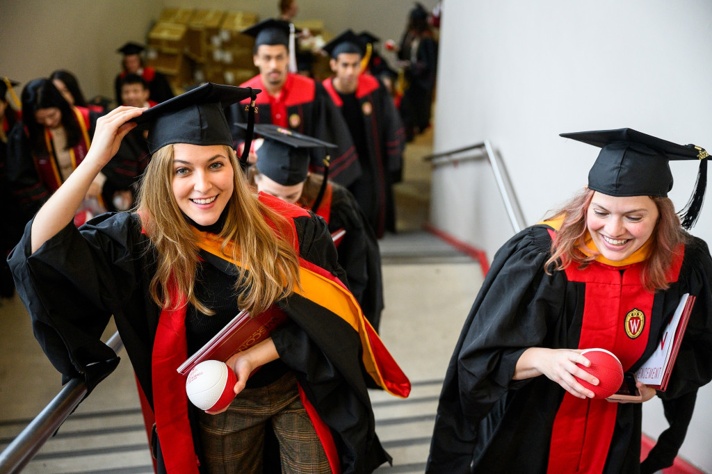 People in commencement robes hold basketballs.