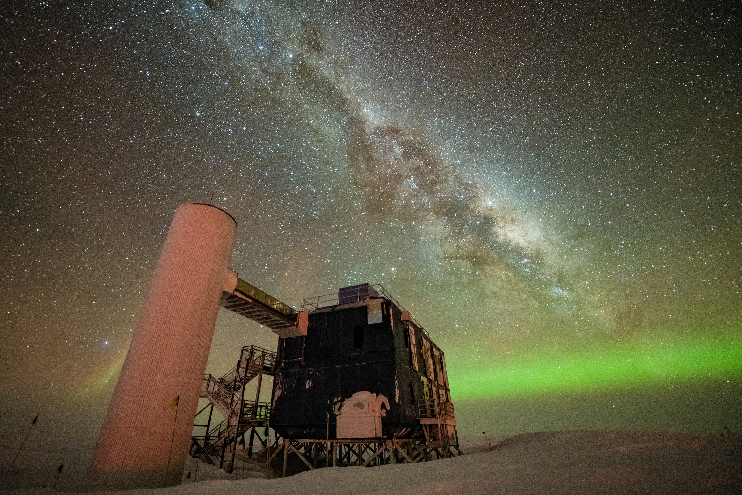 A view of the IceCube Lab with a starry night sky showing the Milky Way and green auroras.