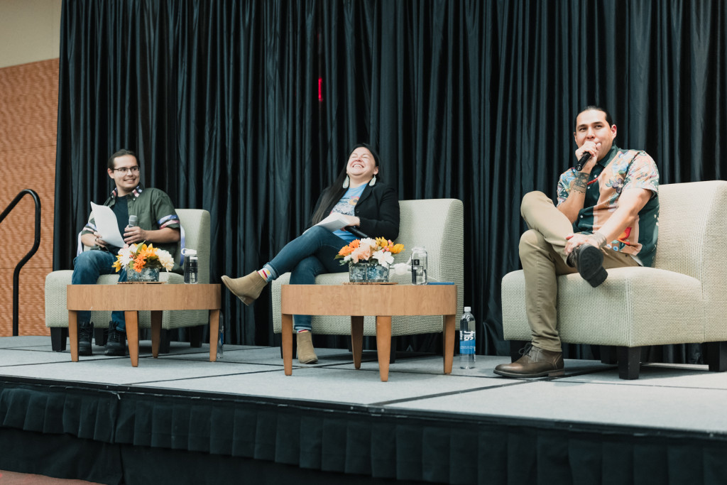 Three people sit on a stage laughing while taking questions from an audience.