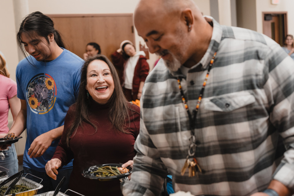 A woman laughs with a colleague while standing in a food line.