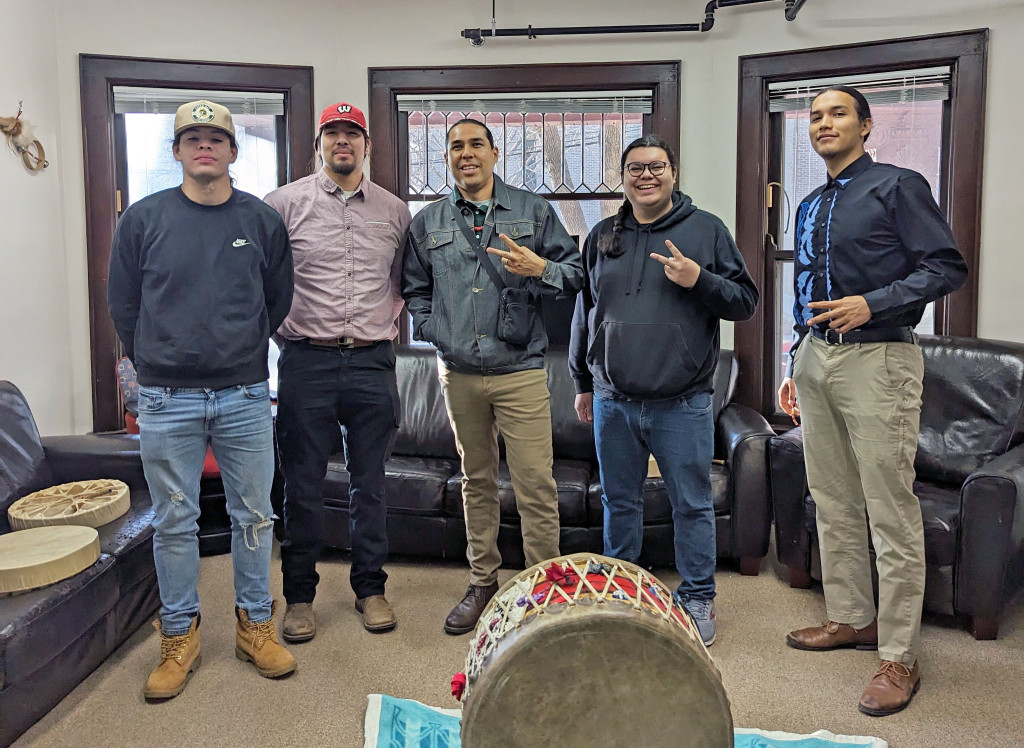 Five people pose for a photo behind a large Tribal drum.