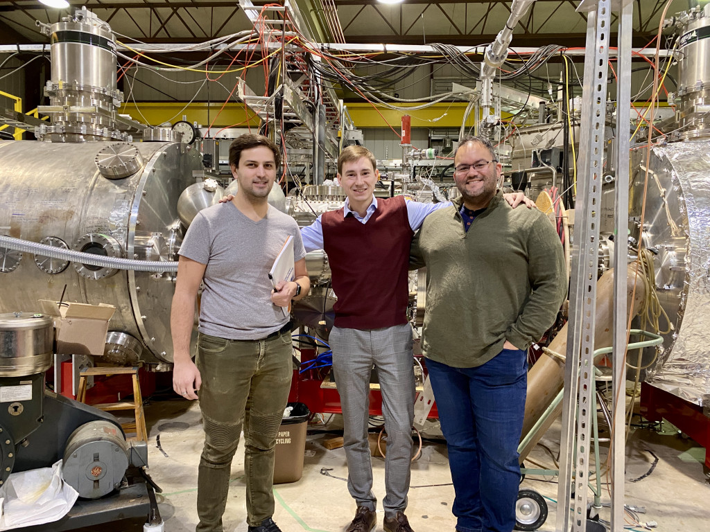 Three people stand arm in arm in front of machinery.