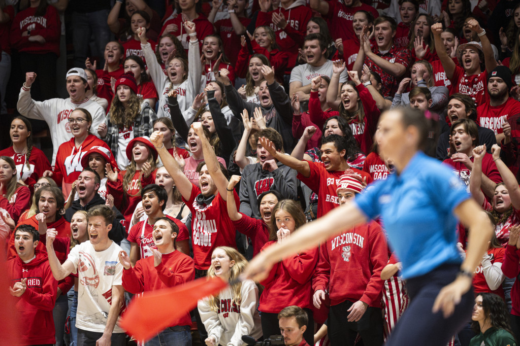 Fans wearing red and white clothes wave their hands and shout.