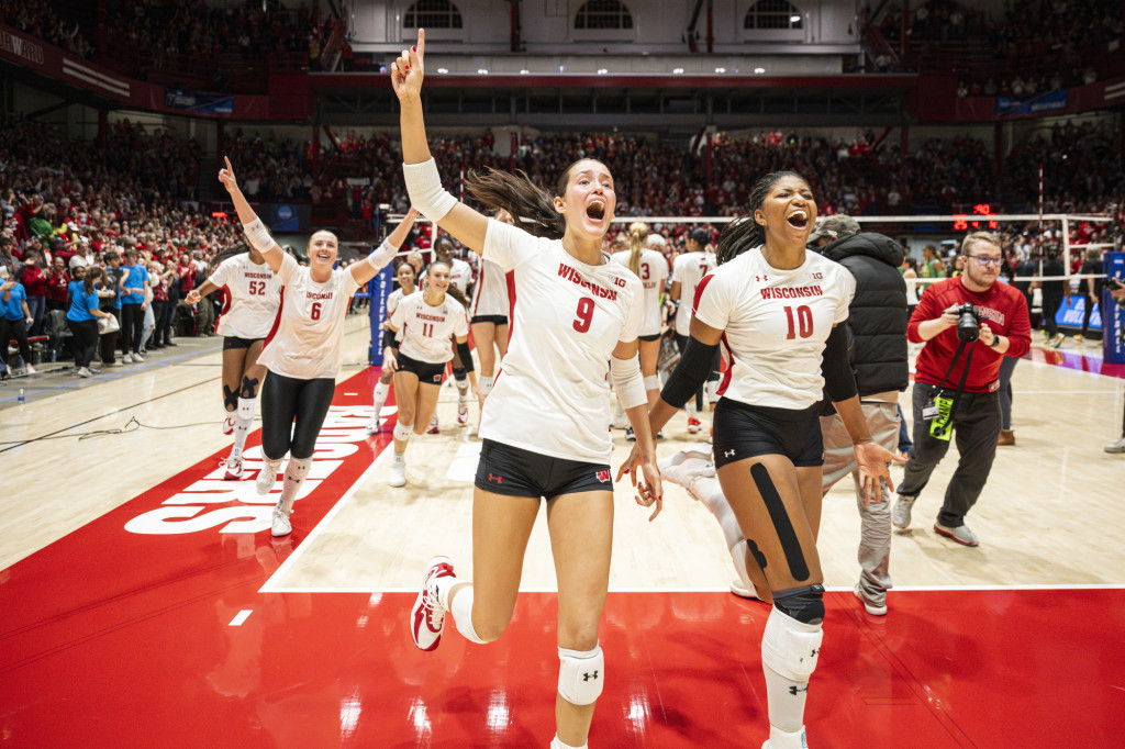 Volleyball players run off the court while smiling and yelling and raising their hands.