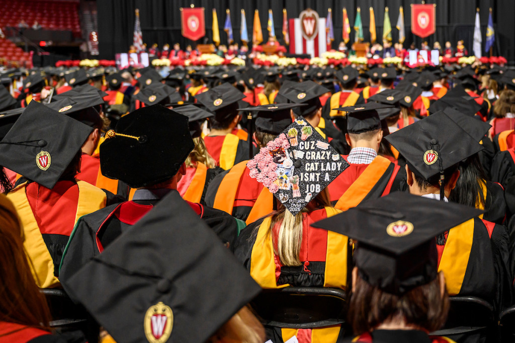 A crowd of people in robes and mortarboard caps stand in an arena.