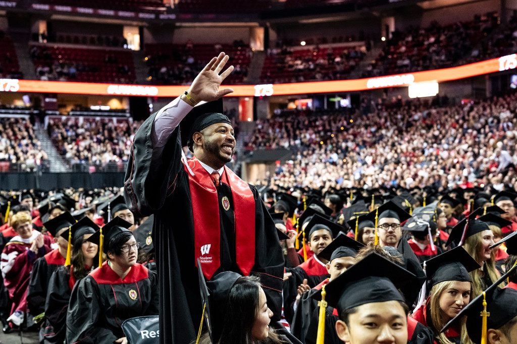 A man stands and waves his hand at the crowd.