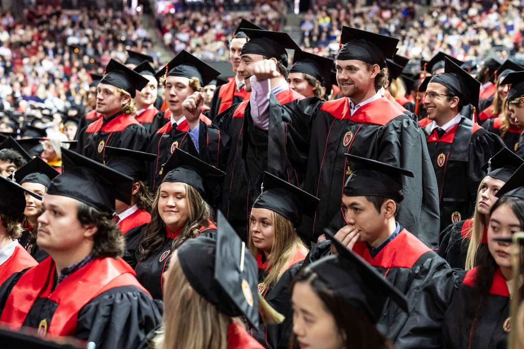 People wearing black commencement gowns gather in a group and cheer.