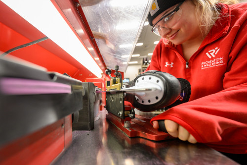 A man holds a hockey skate and brings its blade along a sharpener.