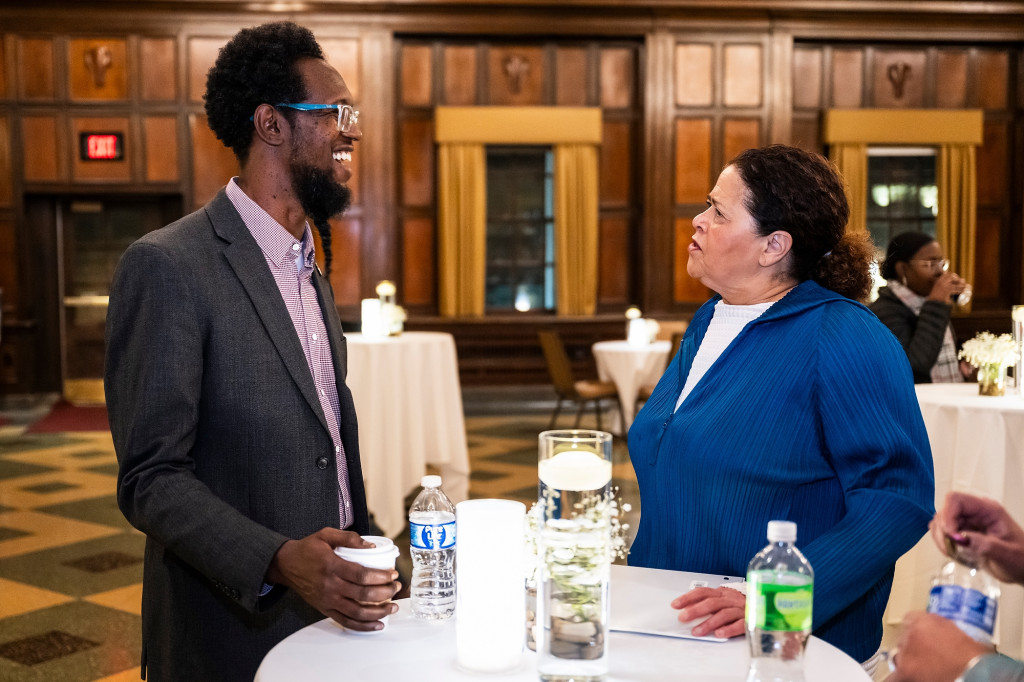 A man and a woman stand at a table and talk.