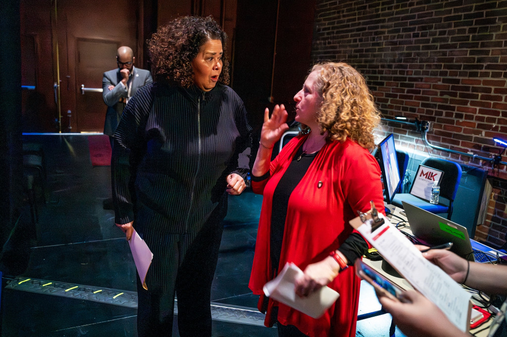 Two women stand close together and talk.