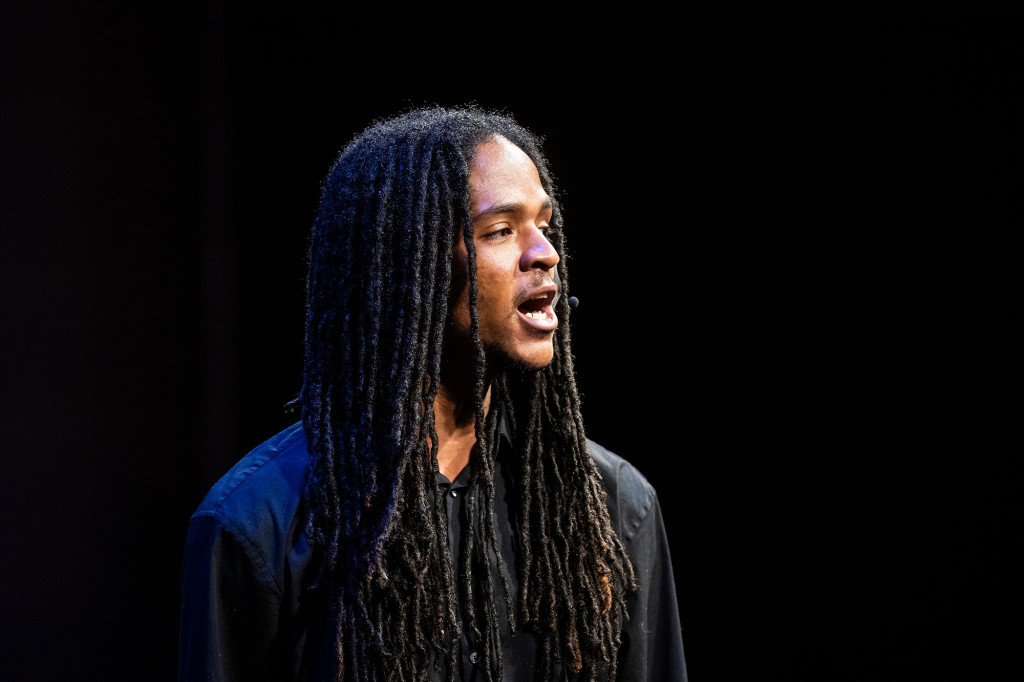 A man speaks on stage, with a black background.